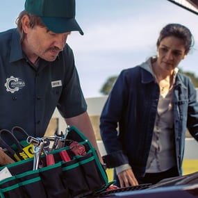 Roadside assistance mechanic standing over a customer's car