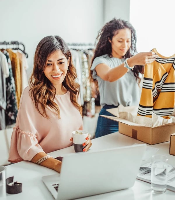 Two retail store employees behind the counter on a laptop and folding a shirt