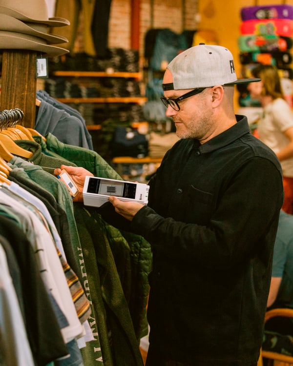 A retail store employee using a Clover Flex to scan the barcode of a shirt on the rack
